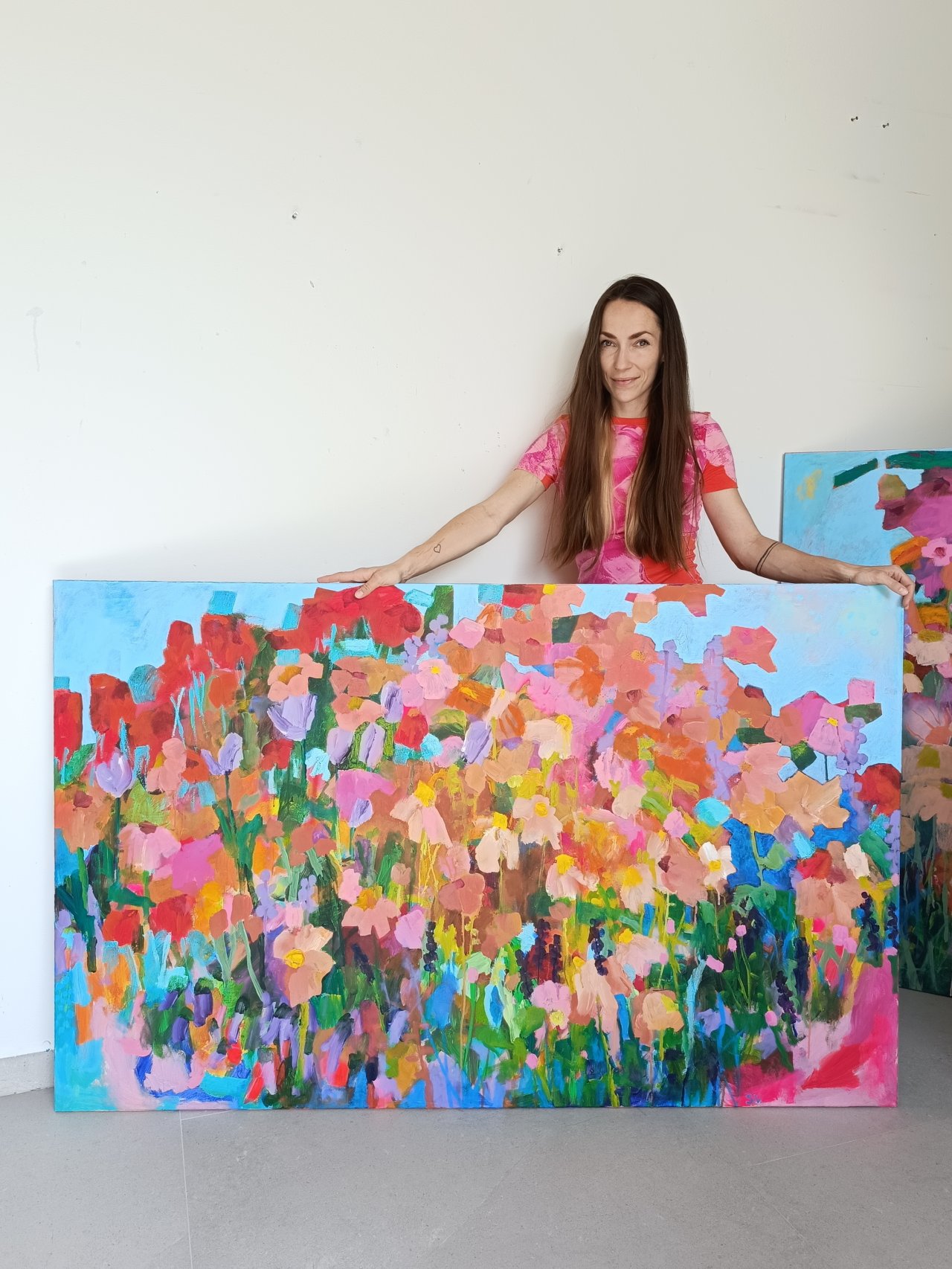 Autorka s abstraktním květinovým obrazem s modrým nebem a jemnými květinami v růžových a béžových tónech