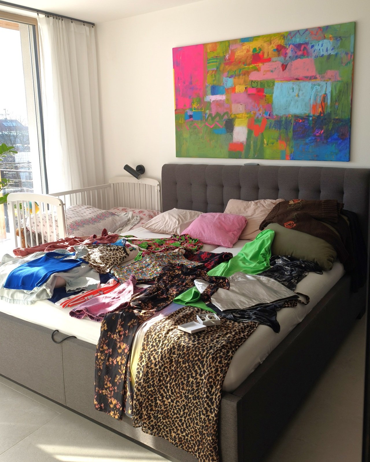 ložnice s abstraktním obrazem Simony Vojtěškové na zdi a oblíbeným oblečením položeným na posteli