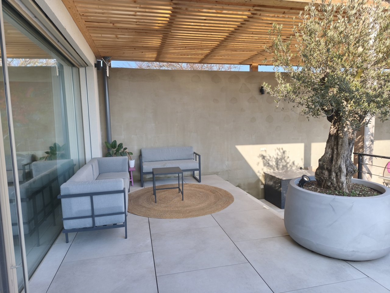 Minimalistická terasa se šedou sedačkou a olivovníkem v květináči