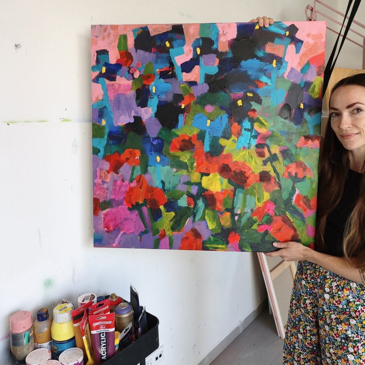 Umělkyně drží modrý abstraktní květinový obraz na plátně o velikosti 80 × 80 cm