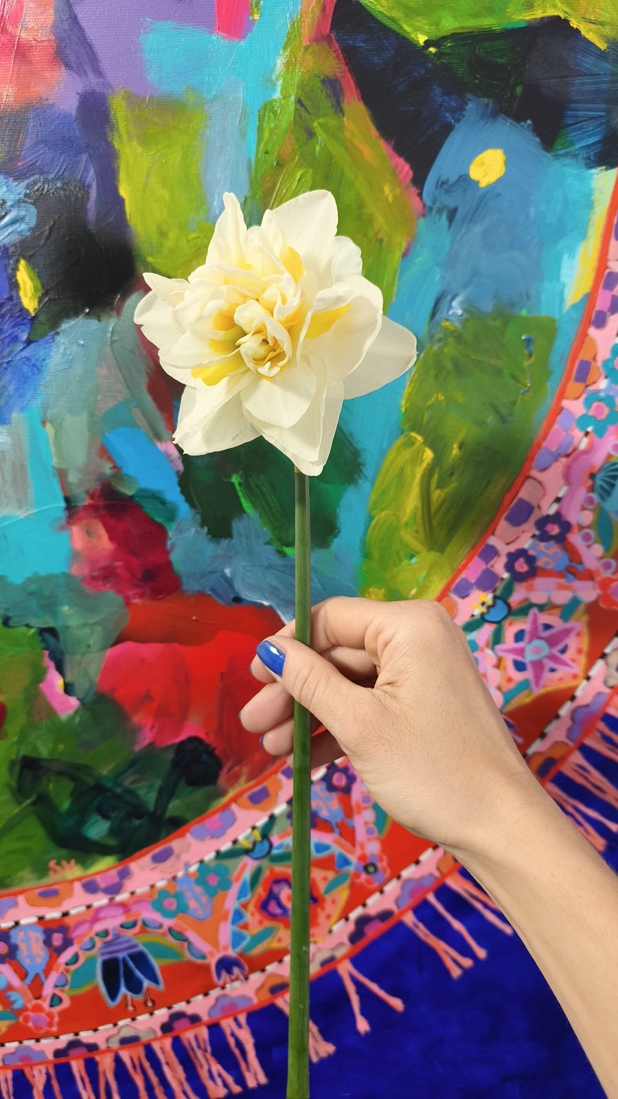 Plnokvětý narcis ze zahrady držený v ruce před abstraktním květinovým obrazem