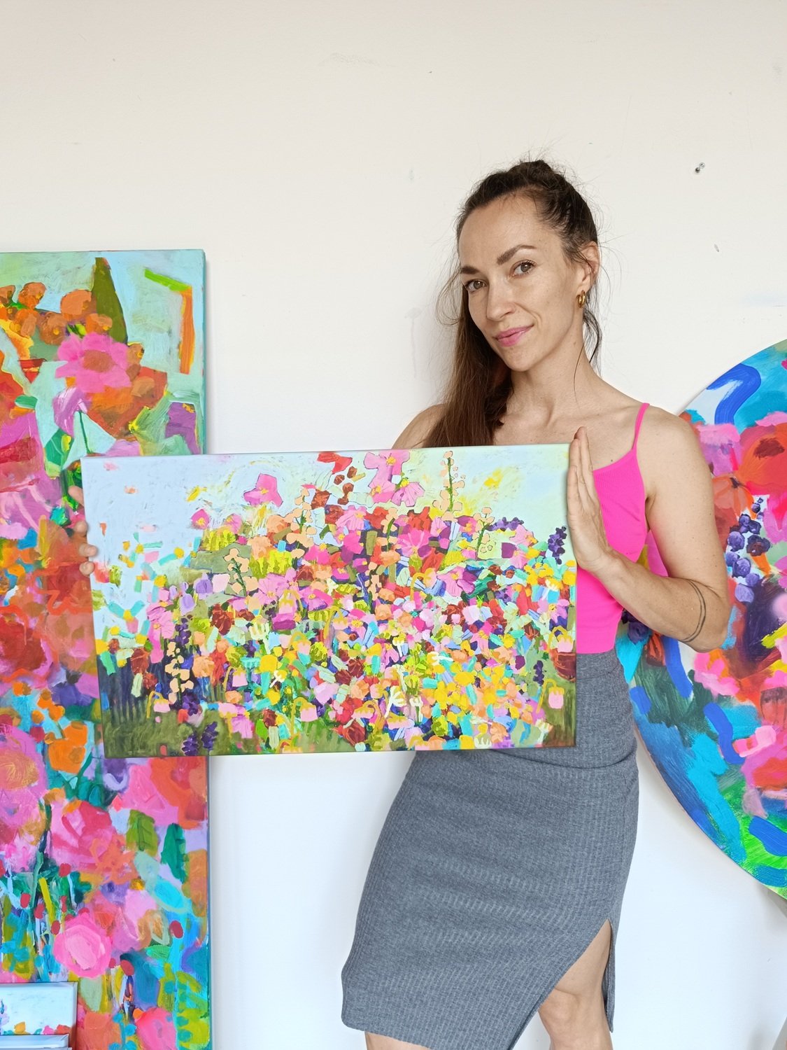 Autorka drží reprodukci abstraktního květinového obrazu inspirovaného loukou, drobné barevné květy a modrá obloha