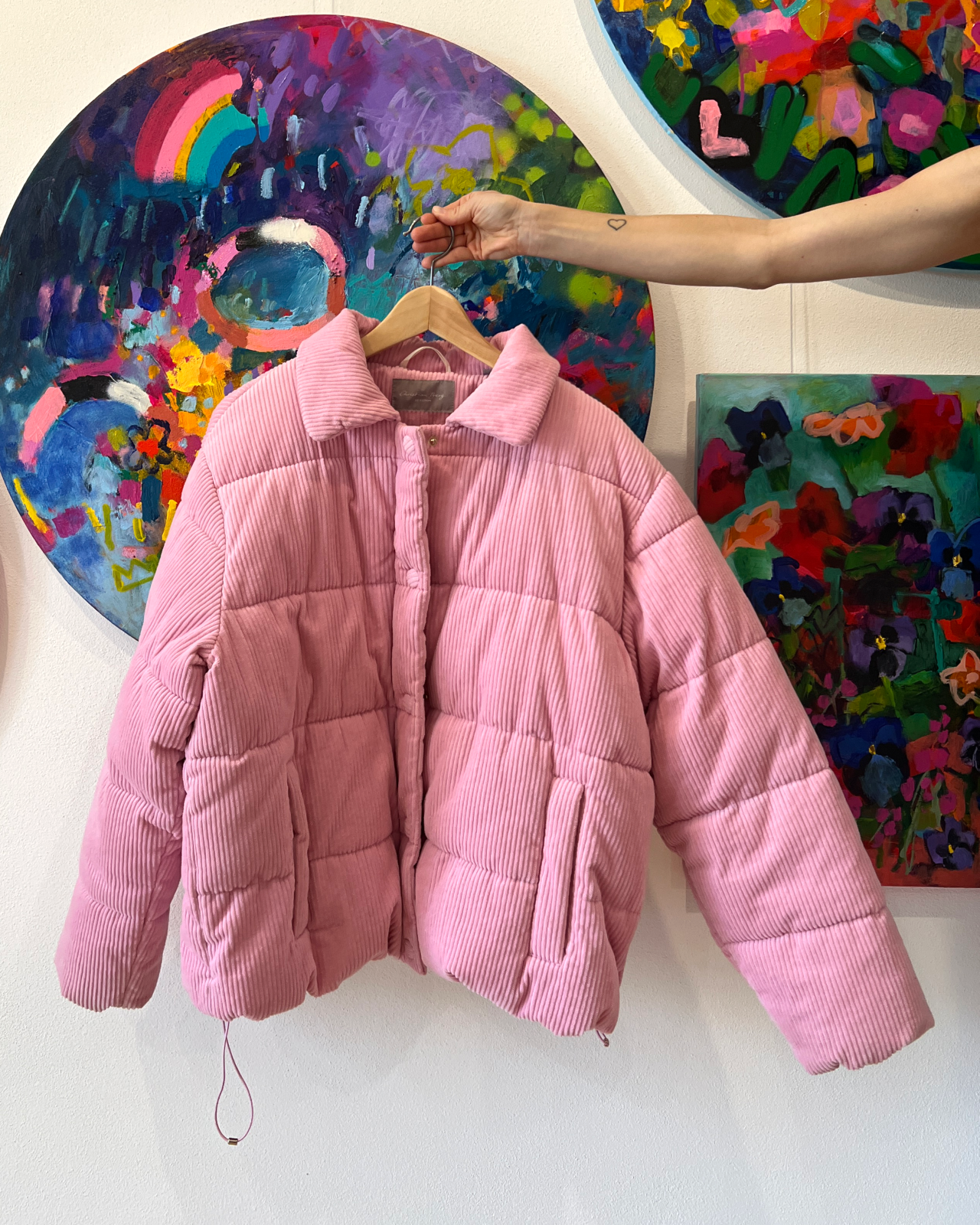 detail růžové manšestrové oversized bundy v interiéru s kulatým abstraktním obrazem na zdi