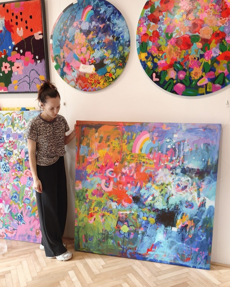 Umělkyně stojí vedle velké reprodukce abstraktního obrazu na plátně o velikosti 130 × 130 cm